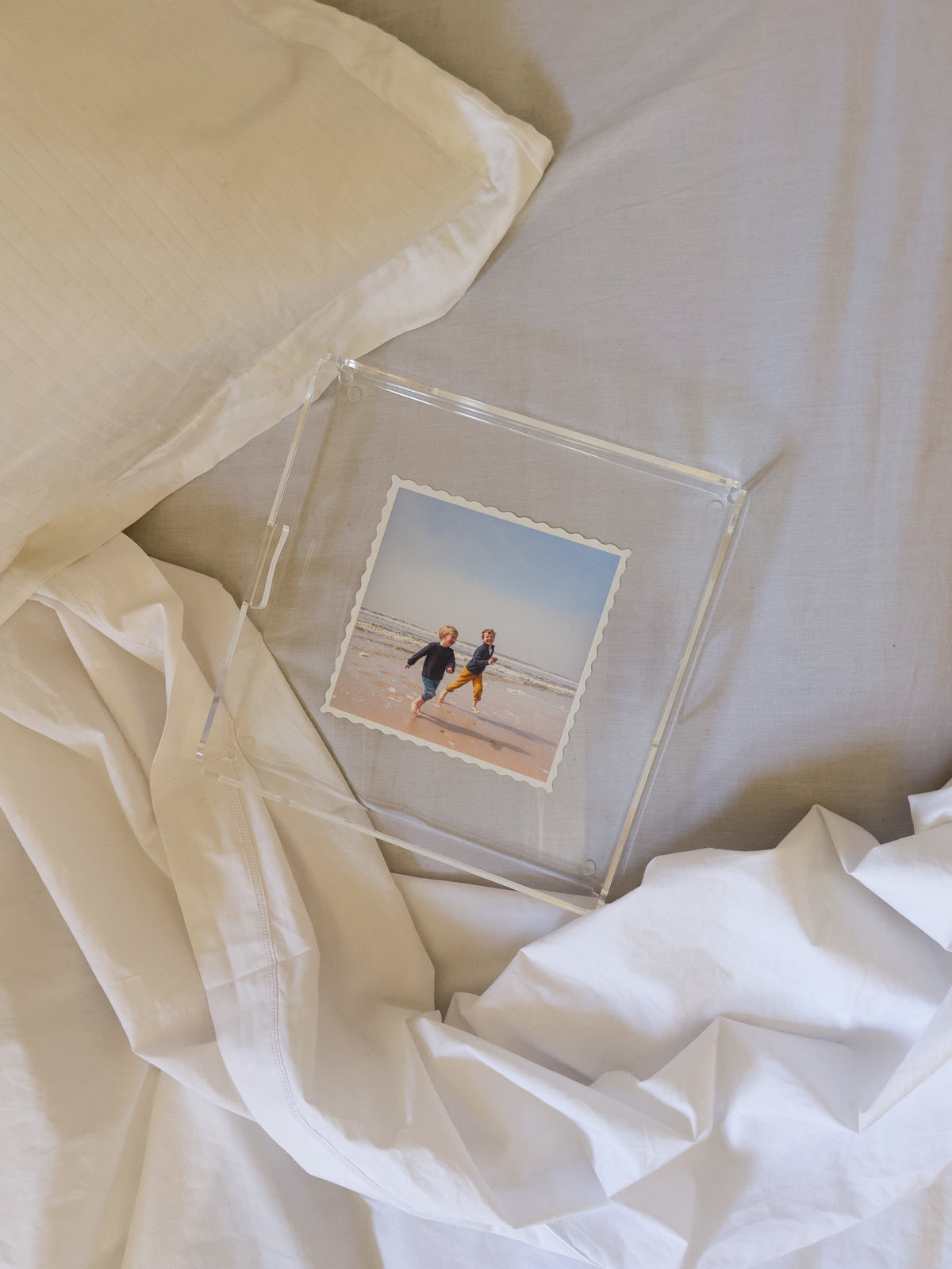 Plateau carré contenant la photo de deux enfants courant sur une plage, posé sur un lit défait