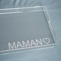 Gros plan sur l'angle d'un plateau en plexi gravé « MAMAN ♡ » en capitales, sur un tissu bleu-gris