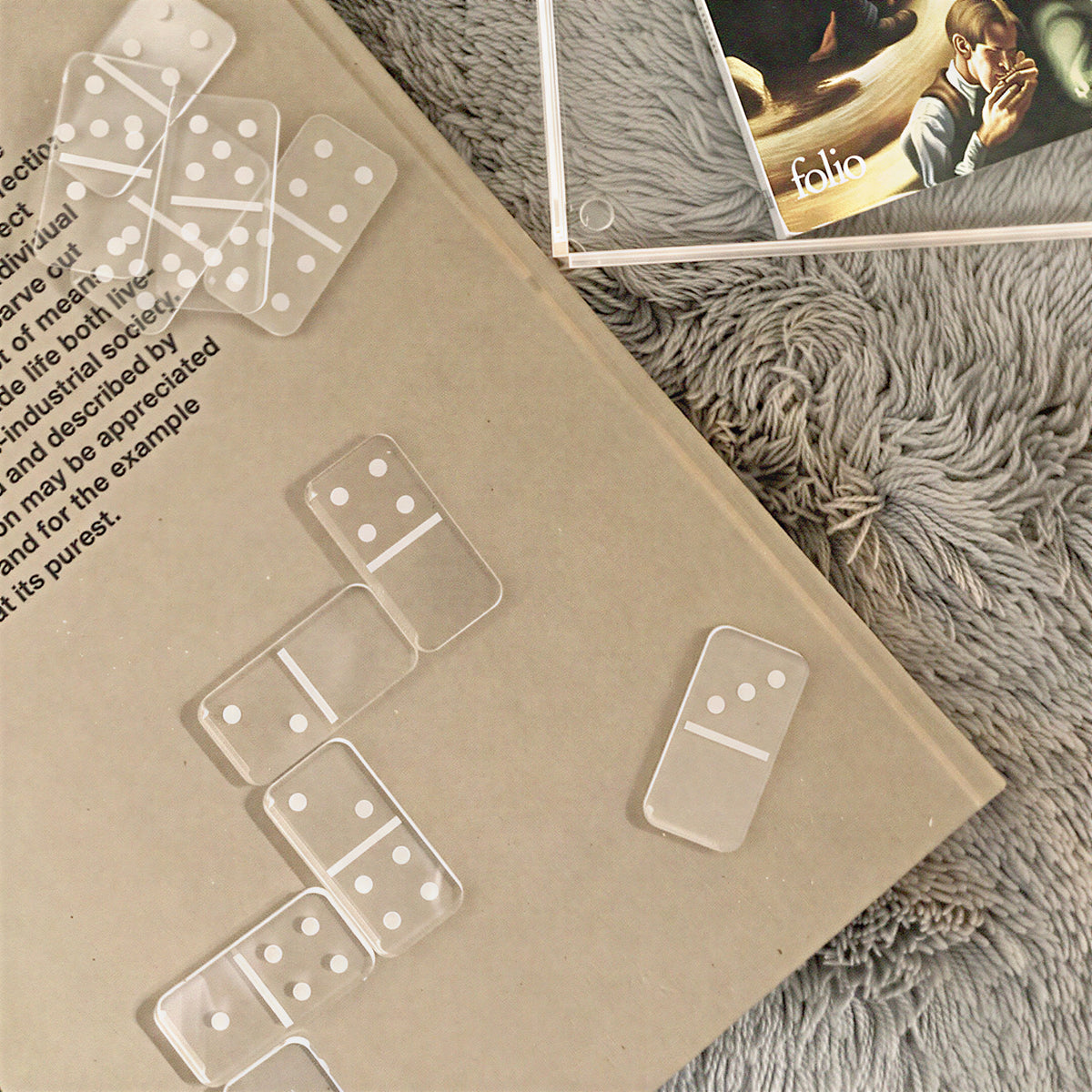 Jeu de dominos en plexi transparent disposé sur un livre à couverture kraft, sur un plaid gris