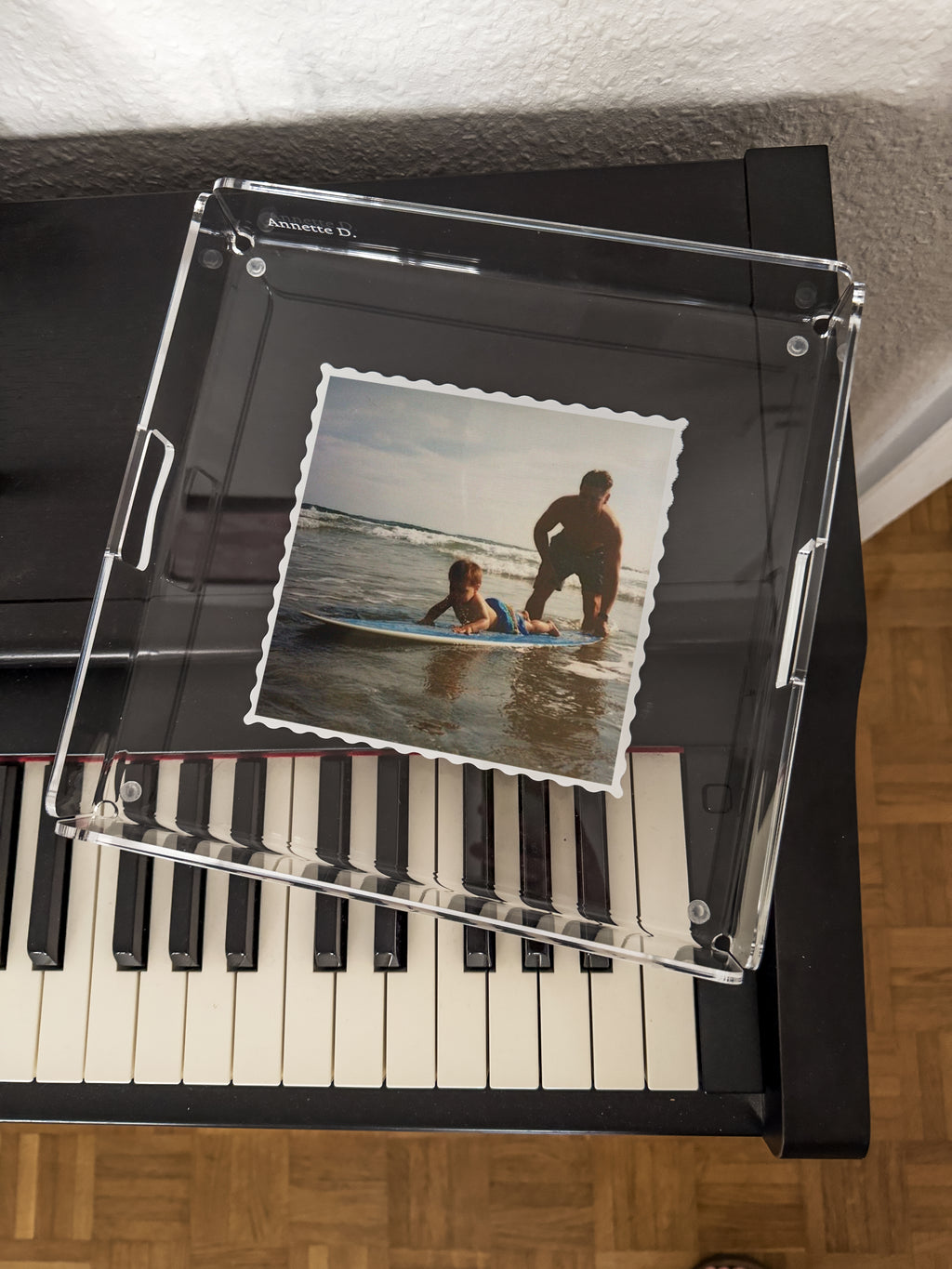 Plateau carré contenant la photo d'un adulte et d'un enfant sur une planche de surf, posé sur un piano