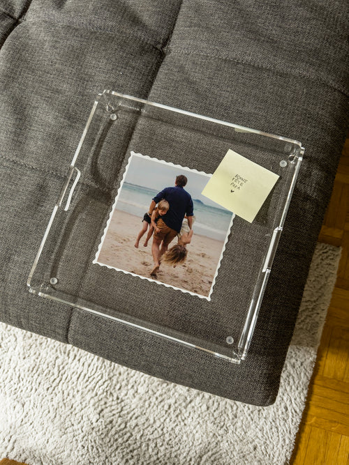 Plateau photo posé sur un pouf en tissu gris, avec un petit mot manuscrit glissé sous le cadre