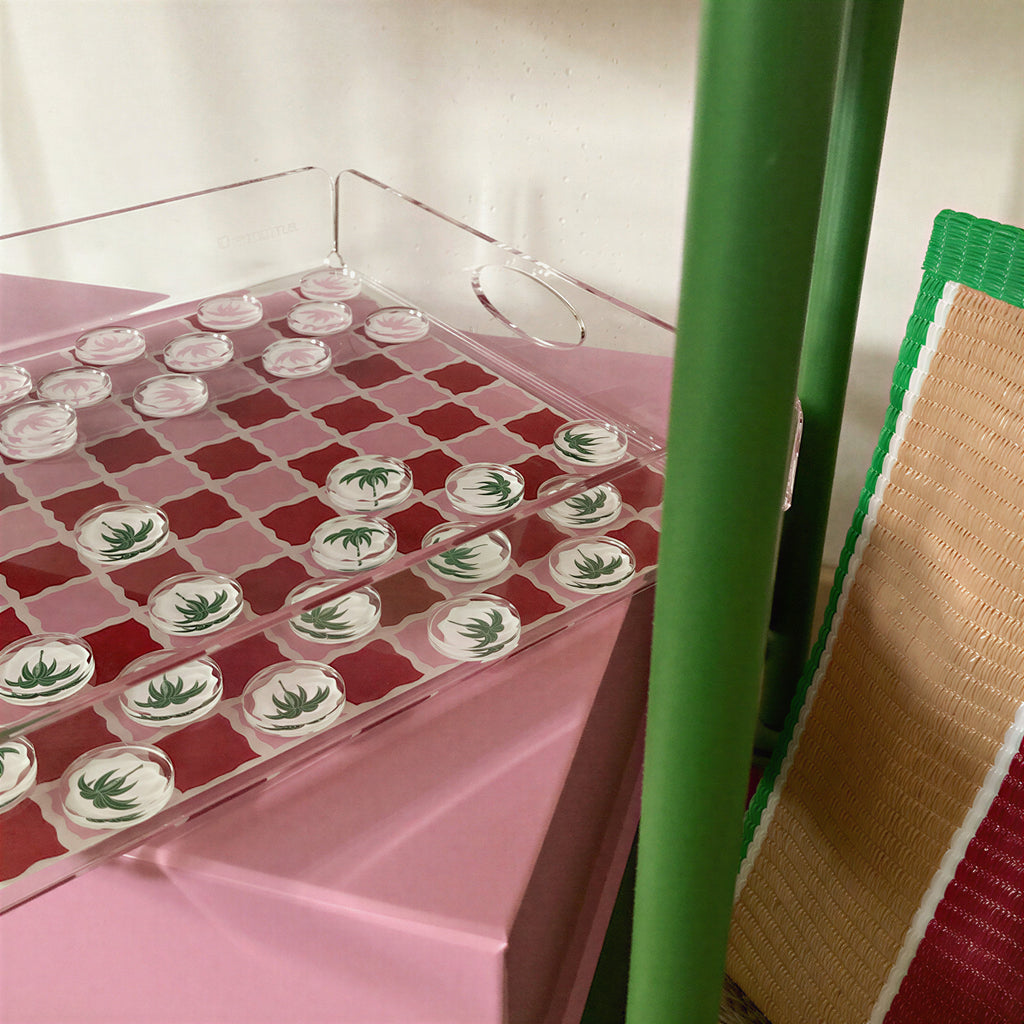 Plateau de jeu de dames rouge et rose vu de trois quarts, pions ornés de palmiers verts