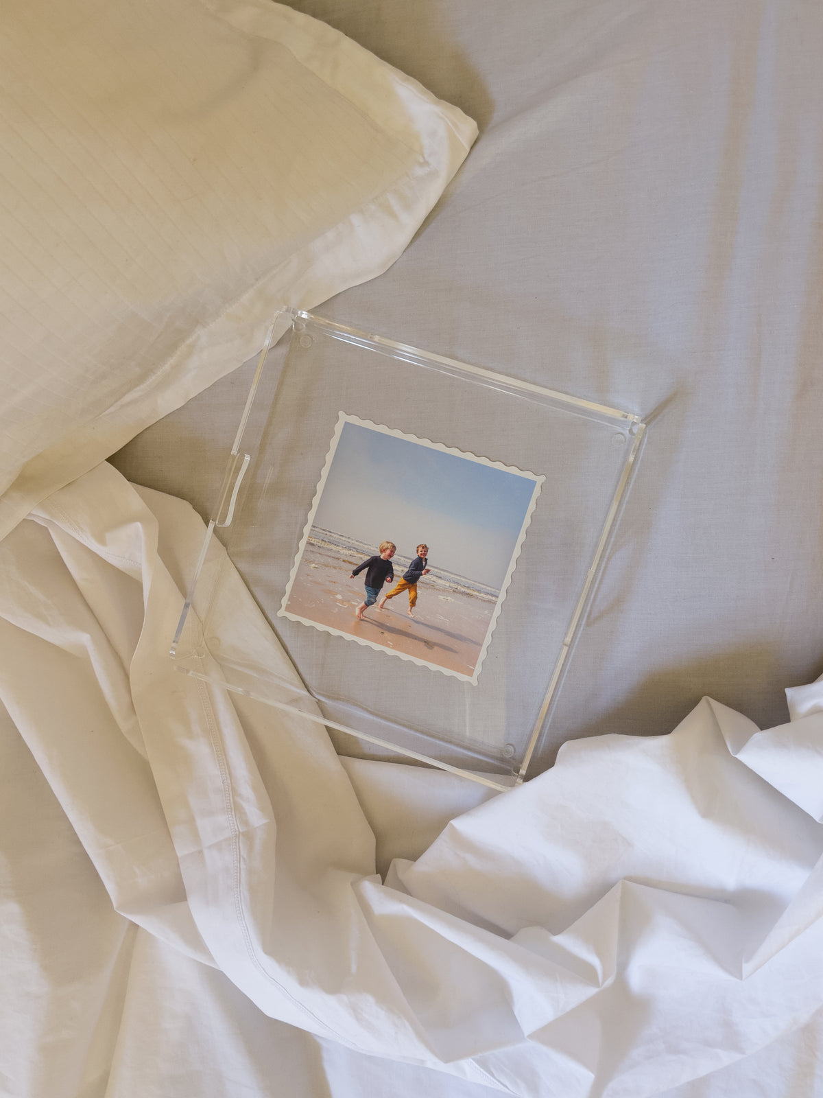 Plateau carré contenant la photo de deux enfants courant sur une plage, posé sur un lit défait