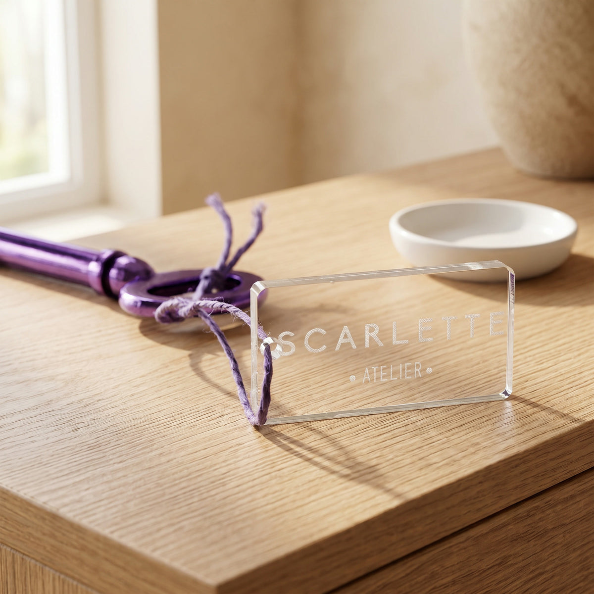 Porte-clé rectangulaire en plexi gravé « Scarlette », attaché à une ancienne clé violette, posé sur une console en chêne près d'une coupelle blanche