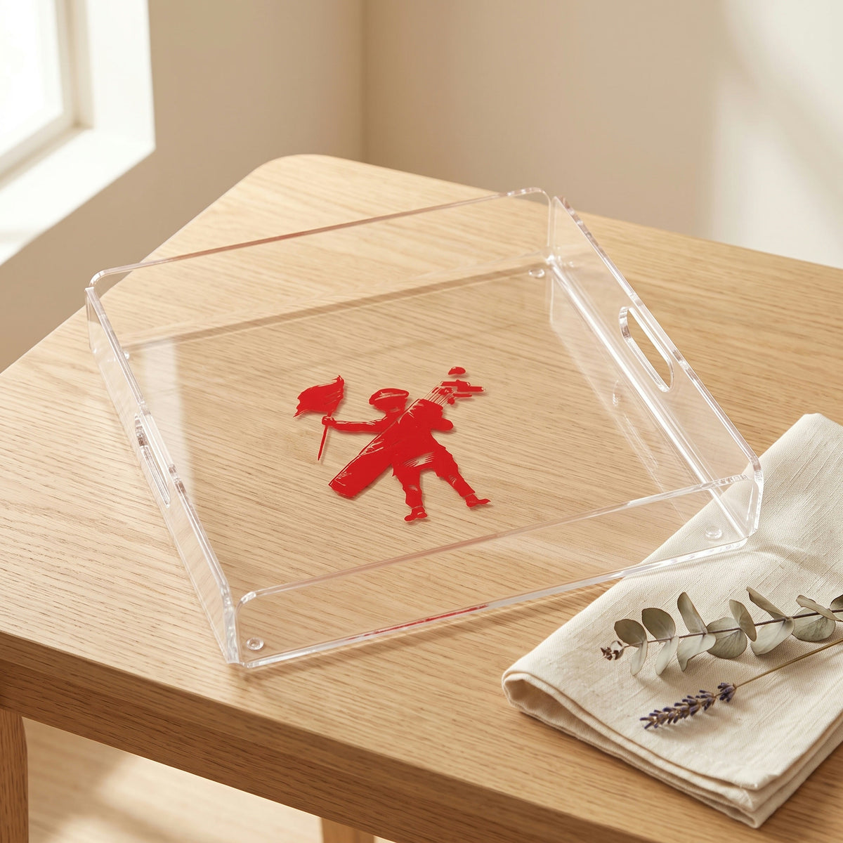 Plateau en plexi imprimé d'un logo rouge, posé sur une table en chêne clair avec une serviette en lin et des fleurs séchées